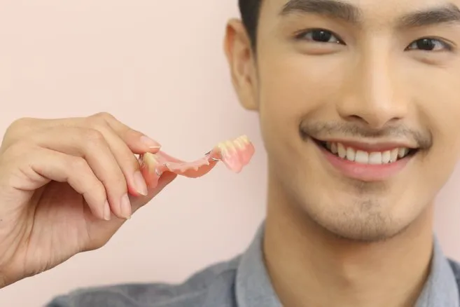 Smiling Man Holding A Pair Of Dentures